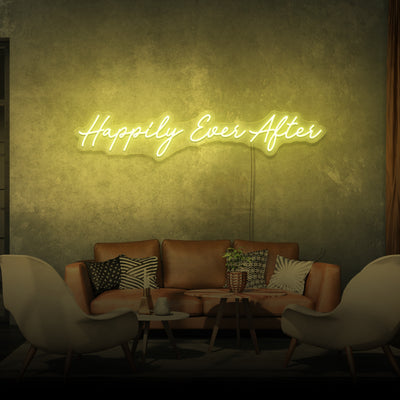 yellow ‘Happily Ever After’ LED neon sign glowing on a wall above a sofa and chairs, with a coffee table, plant, and candles, creating a cozy ambiance. Ideal for wedding decor, bars, or bedrooms, this customizable neon sign by London Neon is both affordable and eco-friendly. Contact us for custom LED neon sign designs or browse our collection in the UK."